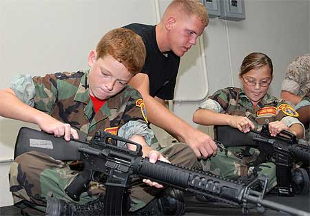 Young Marine instructor Lance Cpl. Donald Slider assists Young Marines Pvt. Adam Kubicki and Pvt. Hannah Baker with their rifles on the indoor simulated marksmanship trainer