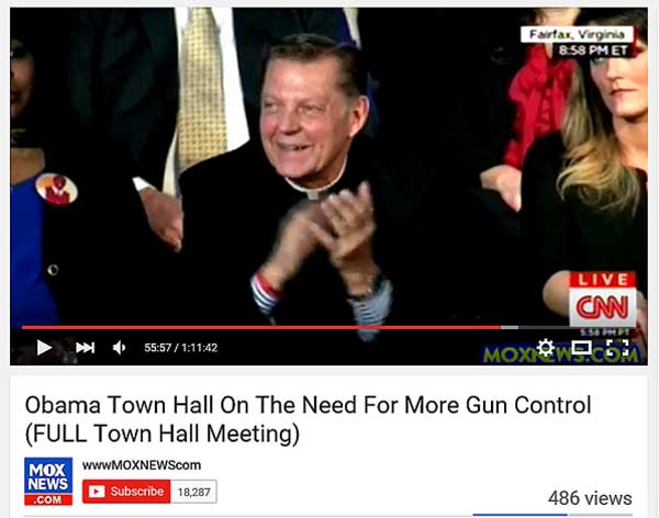 Gun Banner Father Pfleger grinning and clapping.