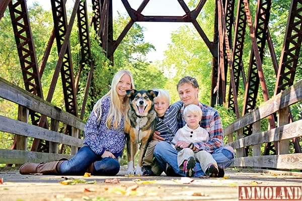 A portrait of a happy family of four people, including mother, father, young child, and baby brother and their pet German Shepherd Mix dog are sitting on an old bridge with the fallen leaves in Autumn.