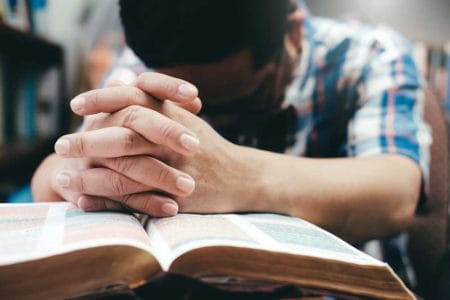 Man Praying Hands Clasped On Bible iStock-938108512