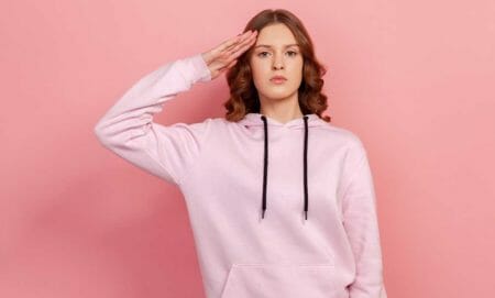 brunette teen girl in hoodie giving salute Draft military iStock-Khosrork 1323294732