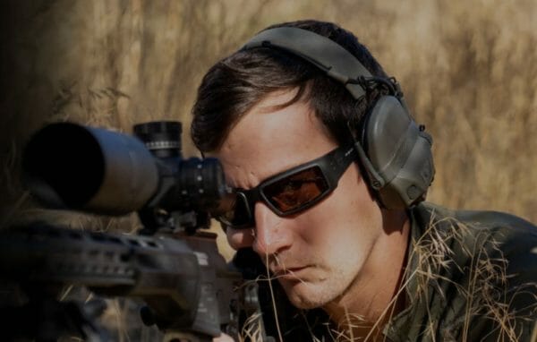 Man holding rifle and wearing Revision glasses outside