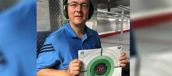 Photo of NSSF President and CEO Joe Bartozzi in a shooting bay at an indoor gun range posing showing the cameraman a freshly shot bullseye target.