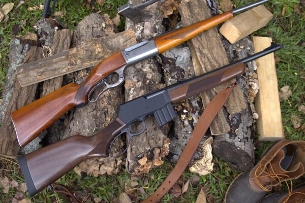 Henry Supreme rifle and a Savage 99 lever action rifle on a wood pile