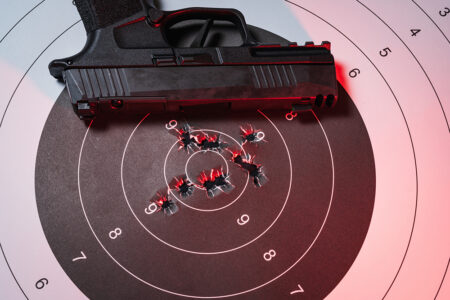 Modern Semi-Automatic Handgun Lying on a Paper Shooting Target with Multiple Bullet Holes in the Center Bullseye After Target Practice.Close up photo iStock-2260077315