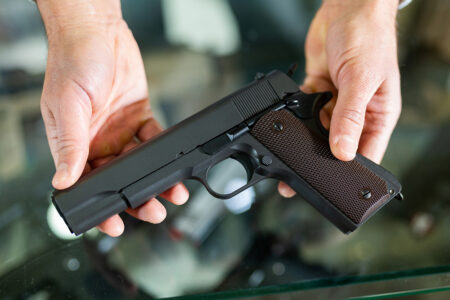 Gunsmith shop assistant demonstrates black pistol in hands stock photo iStock-1398682785