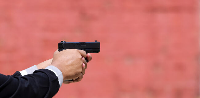 Close up view of hand holding a pistol / handgun taking aim for target. iStock-1175500022