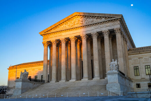 The United States Supreme Court Building at sunset, partly in a shadow cast by the Capitol building, with afternoon light illuminating columns and the "Equal Justice Under Law" pediment sculptures