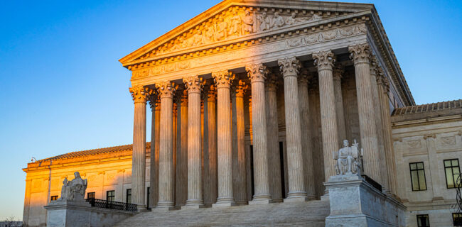 The United States Supreme Court Building at sunset, partly in a shadow cast by the Capitol building, with afternoon light illuminating columns and the "Equal Justice Under Law" pediment sculptures