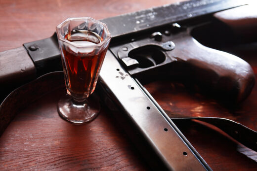 Old USA submachine gun closeup near glass of whiskey on wooden background iStock-985233138