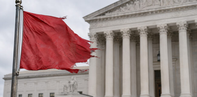 Distressed red flag flying in front of a courthouse, symbolizing red flag gun laws and due-process concerns.