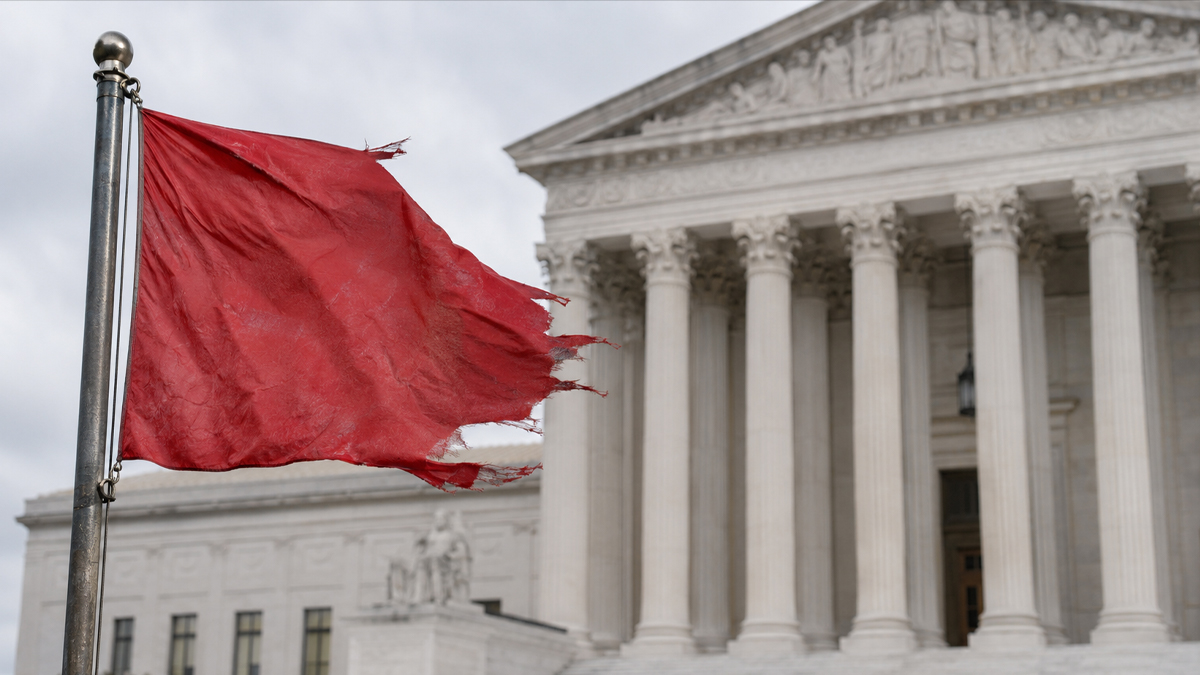 Distressed red flag flying in front of a courthouse, symbolizing red flag gun laws and due-process concerns.